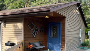 Une cabane en bois avec une porte bleue, un banc et un barbecue à l’extérieur.