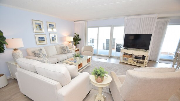 A living room with a sofa, armchairs, a coffee table, a TV, and a balcony with a view. - Harbour Island 103L-Baywater 14th St, WIFI, Pool, Elev, W/D, AC (Ocean City)