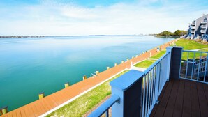 A waterfront balcony with a view of calm water, a wooden deck, and a grassy area. - Harbour Island 103L-Baywater 14th St, WIFI, Pool, Elev, W/D, AC (Ocean City)