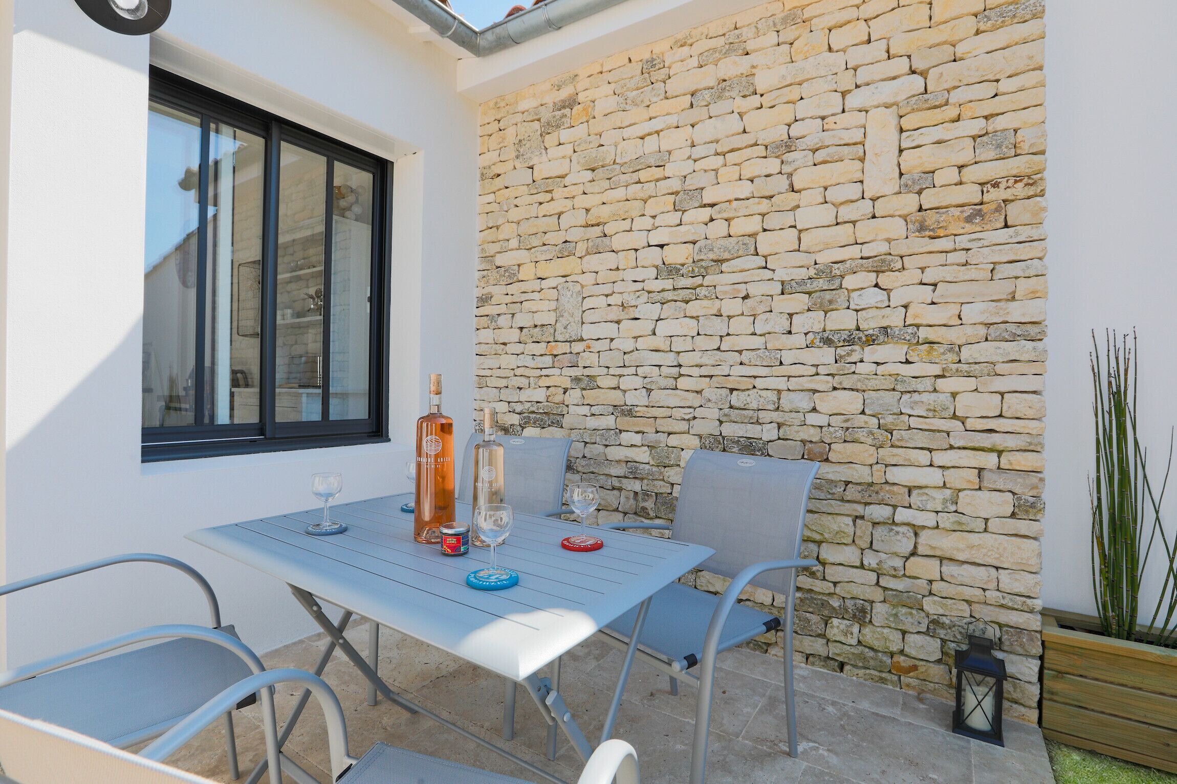 Eine Terrasse mit Steinmauer, einem Tisch mit Stühlen und einer Flasche Alkohol.