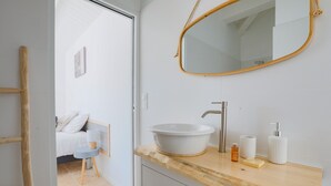Ein Badezimmer mit einem Holzkosmetikschrank, einem weißen Waschbecken, einem Spiegel und Pflegeprodukten.