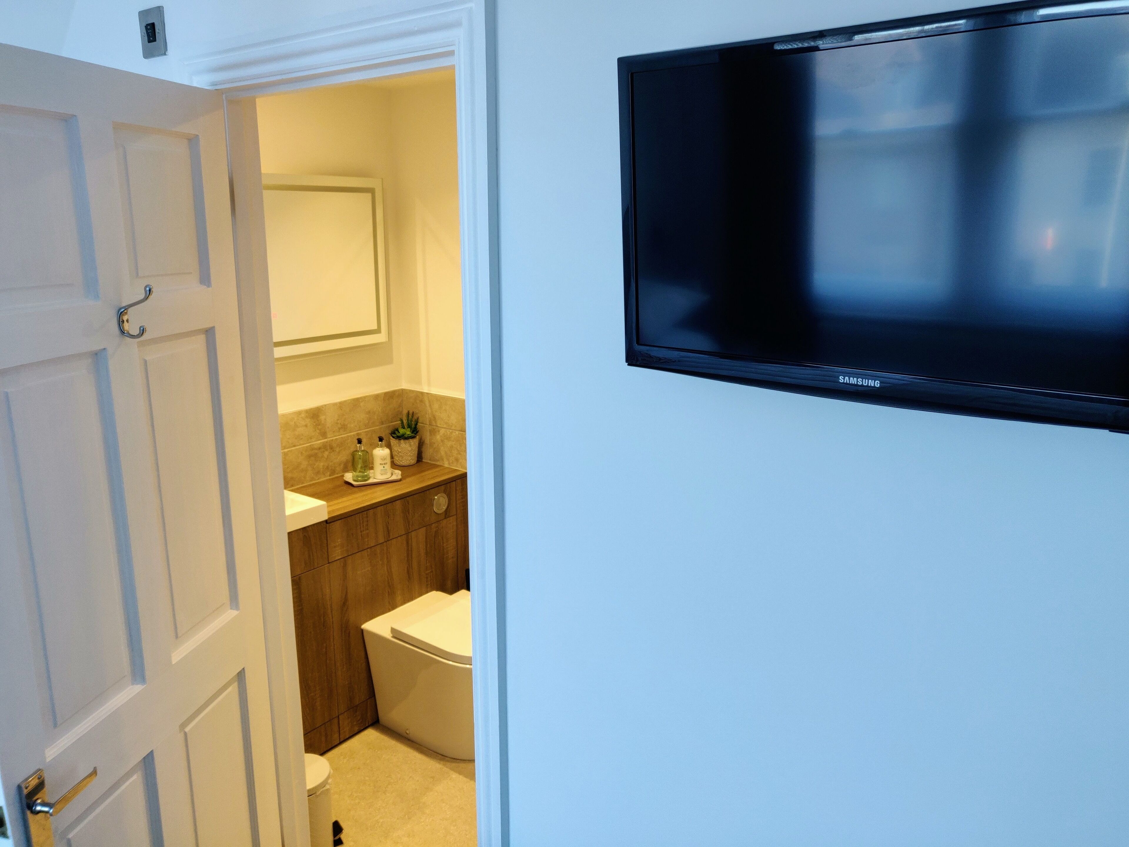 A bathroom with a toilet, sink, and a Samsung TV mounted on the wall.