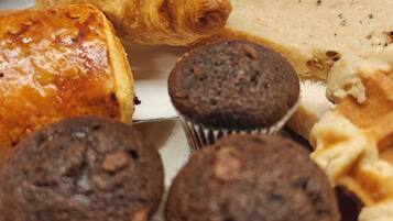 Diversos produtos de panificação em uma bandeja, incluindo croissants, muffins e uma barra de pão.