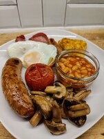 Un plato de comida para el desayuno con salchichas, huevos, champiñones, frijoles al horno y un tomate.