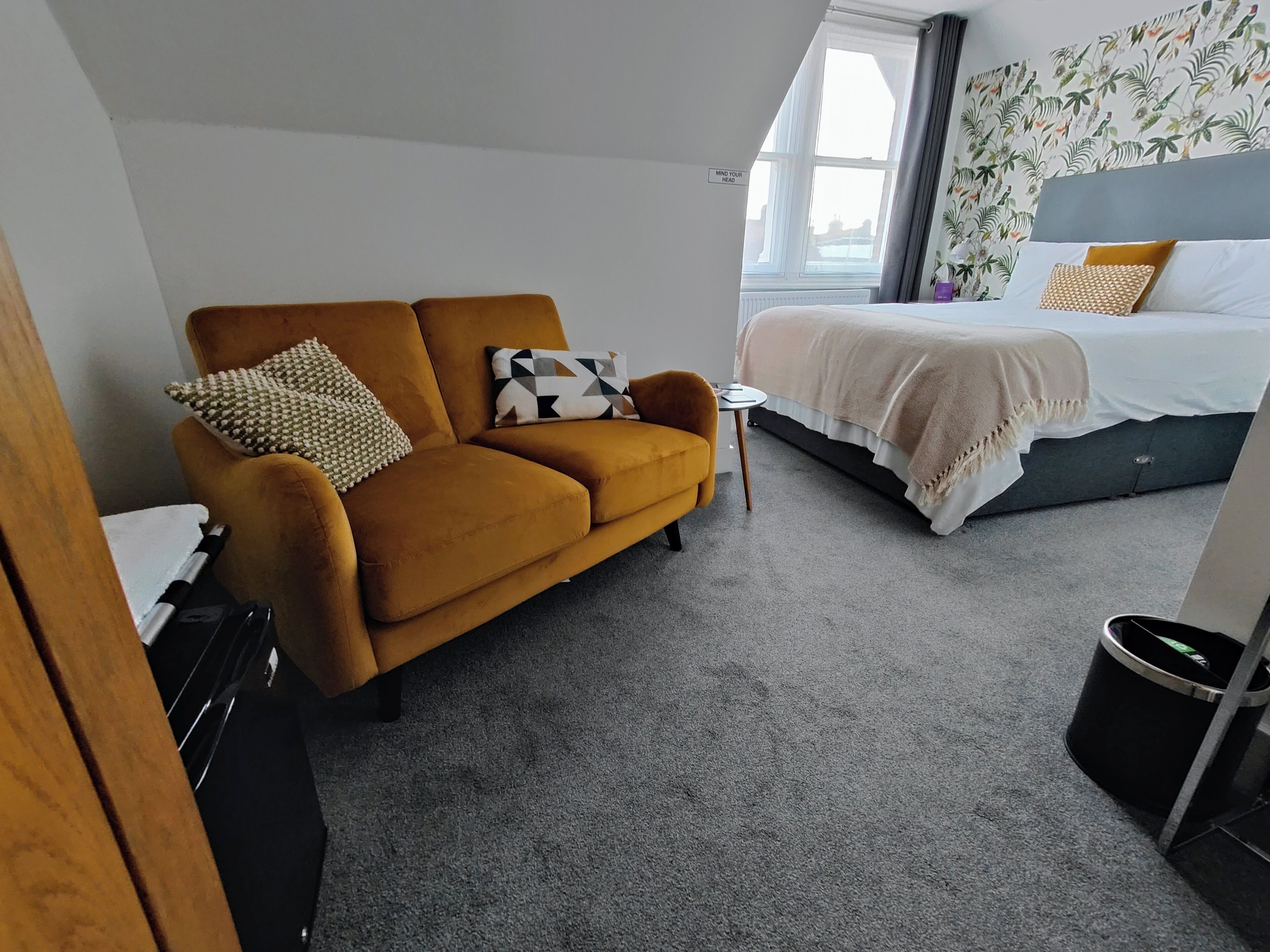 A hotel room with a sofa, a bed, a small table, and a window.