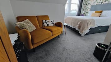 A hotel room with a sofa, a bed, a small table, and a window.