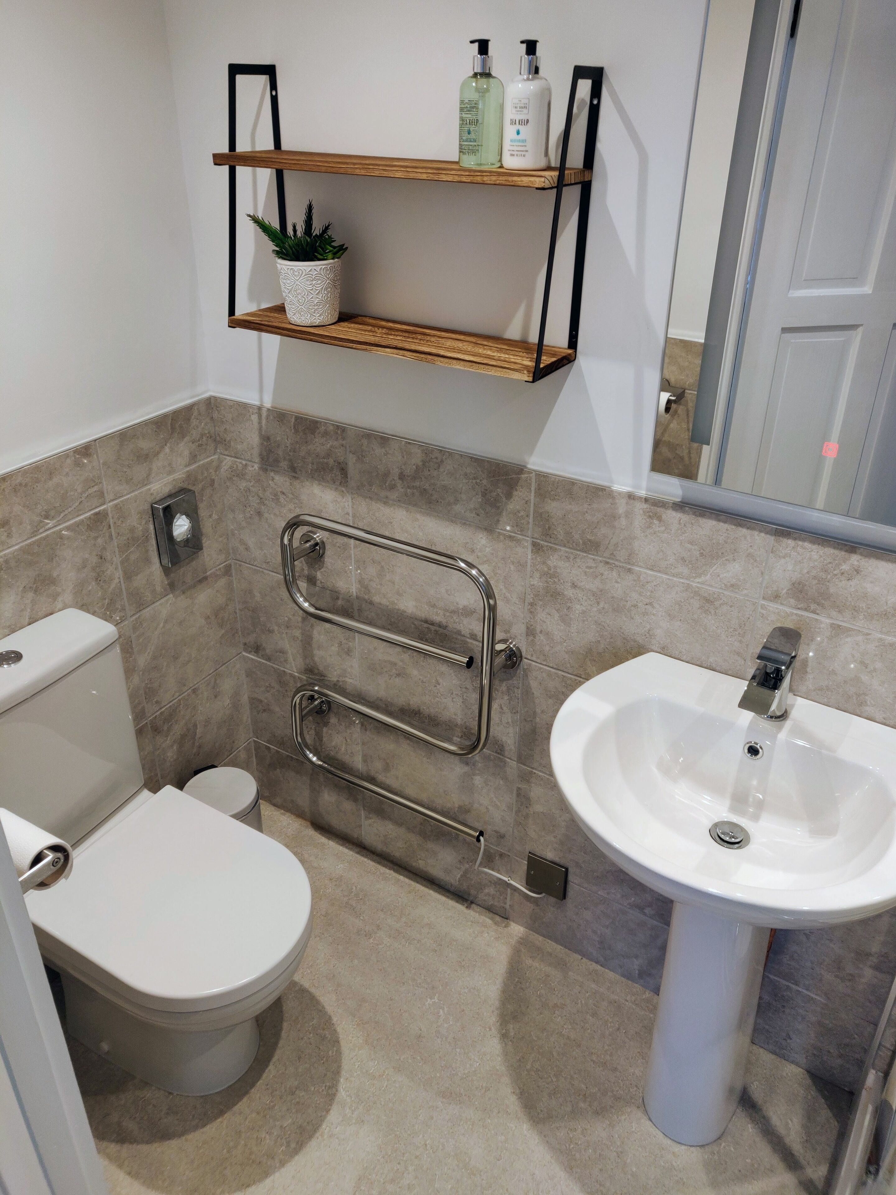 A bathroom with a toilet, sink, and shelves with toiletries.