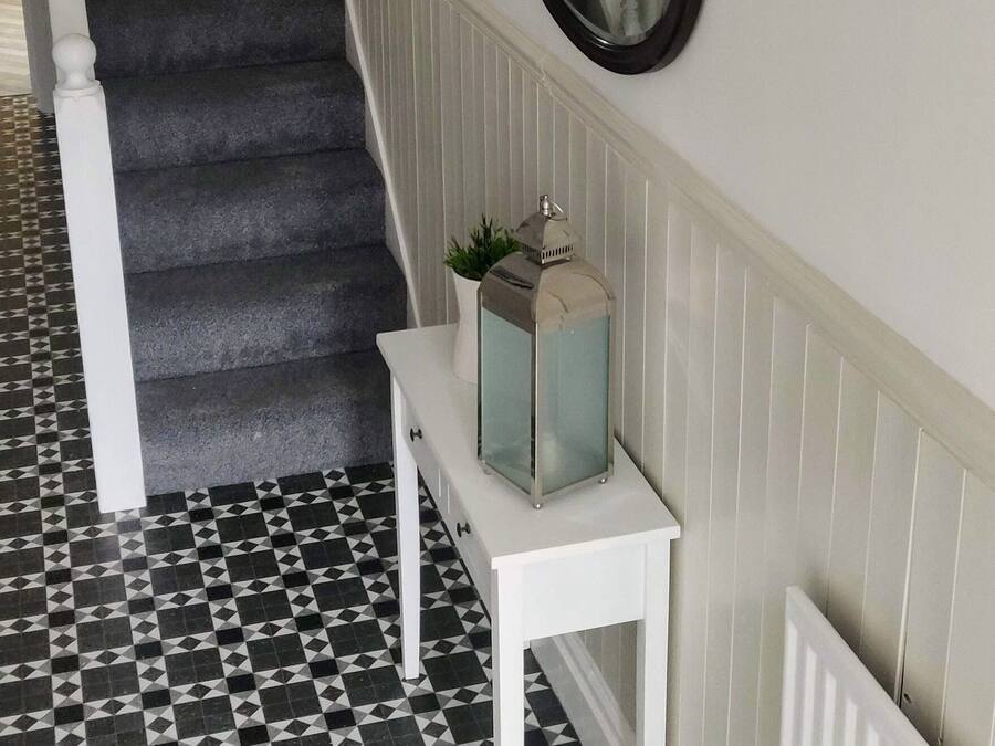 A staircase with a black carpet, a white console table with a mirror and a plant, and a patterned floor.