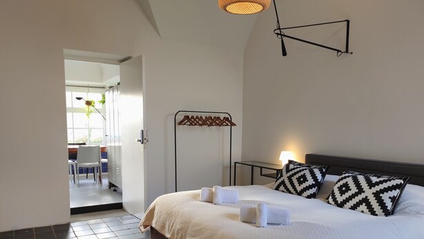 Een keurig opgemaakt slaapkamer met een bed, kussens, een nachtkastje en een vloerlamp.