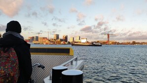 Een uitzicht op het water met een stadsgezicht op de achtergrond, inclusief gebouwen en een kraan.