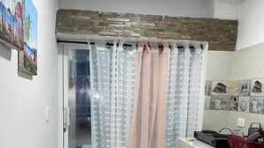 A kitchen with a stone backsplash, a white countertop, and a sliding glass door with sheer curtains. - Welcome to real paradise (San Luis)