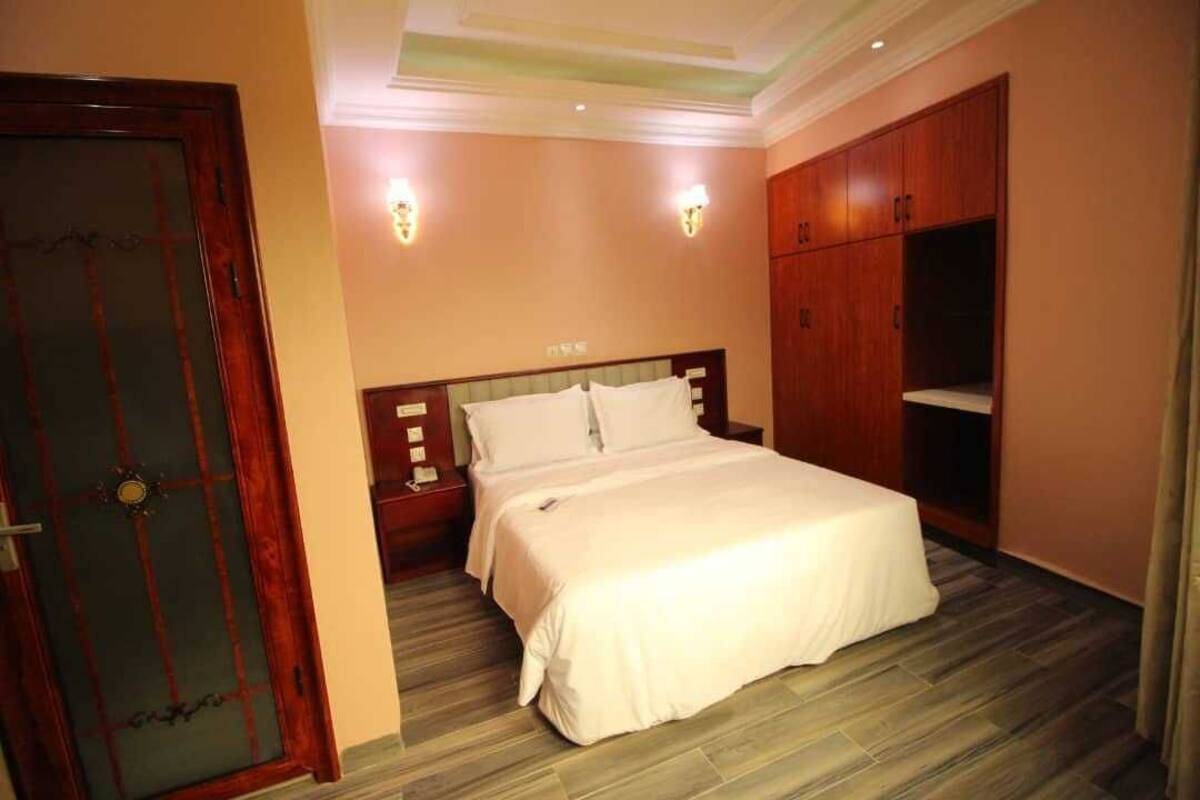 A hotel room with a bed, wooden wardrobe, and two wall-mounted lights.