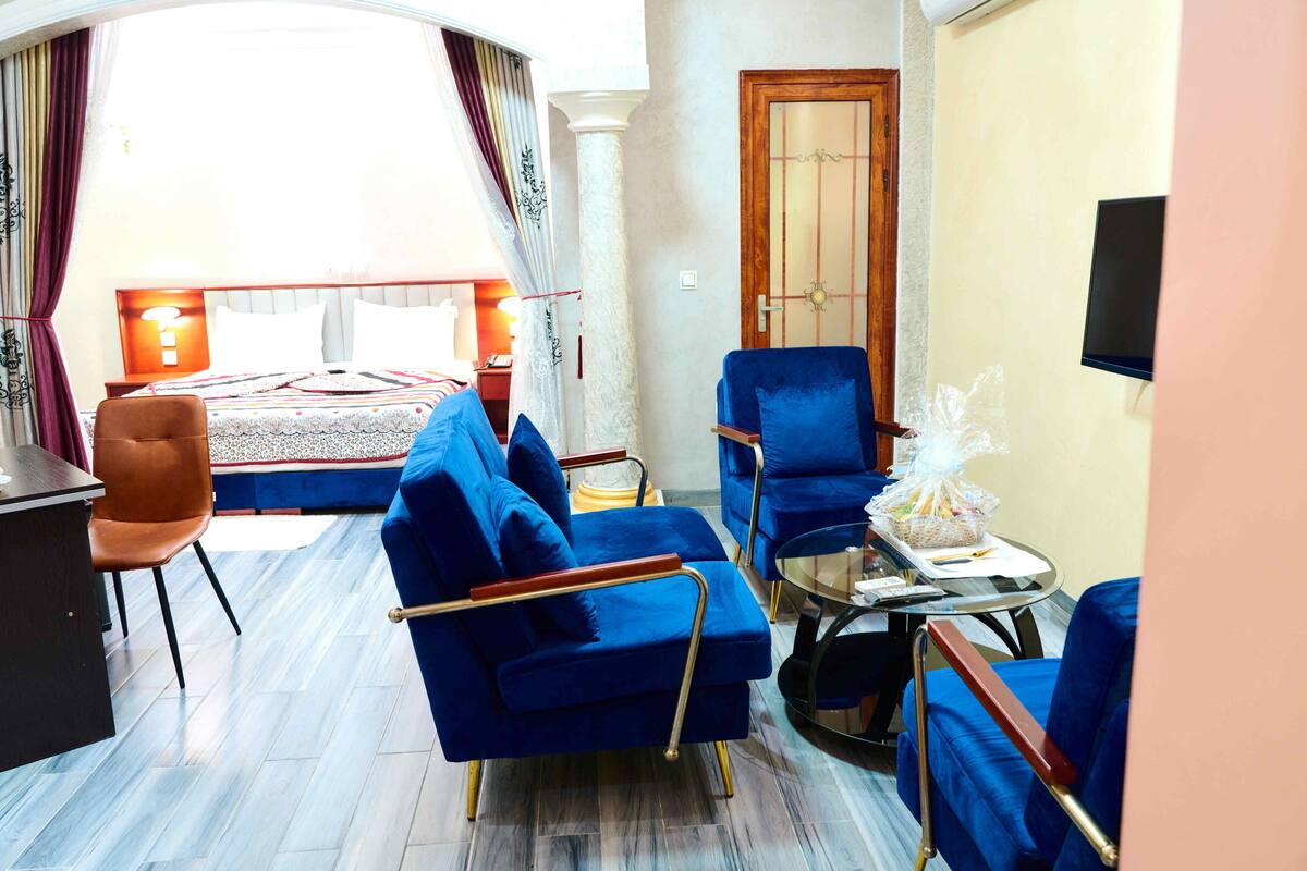 A hotel room with a bed, two blue armchairs, a small table, and a TV.