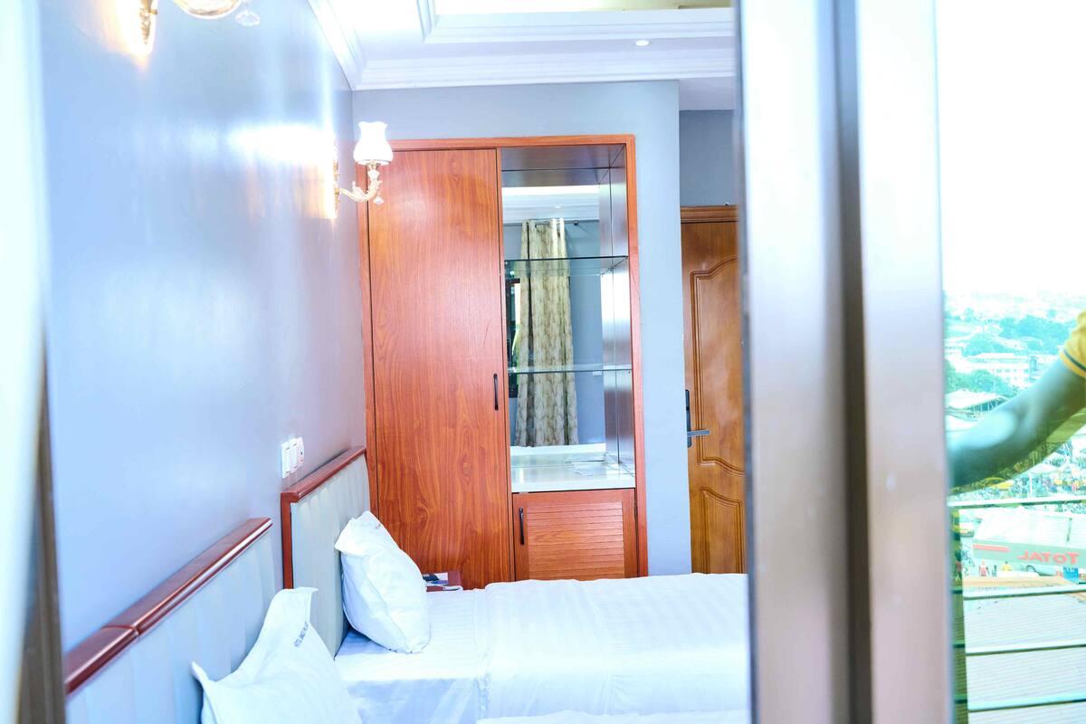 A hotel room with a bed, a wooden wardrobe, and a mirror.