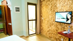 A hotel room with a wooden floor, a bed, a television on a stand, and a door leading to a balcony. - Sindz Palace Hotel (Yaoundé)