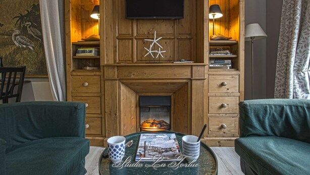 Una sala de estar acogedora con chimenea, paneles de madera, un televisor de pantalla plana y dos sillones verdes.