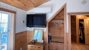 Een houten interieur met een aan de muur bevestigde televisie, een houten dressoir met spiegel en een houten trap.