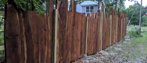 A wooden fence with vertical slats and a metal bottom rail, running alongside a dirt path with sparse vegetation.