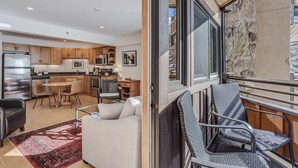 Une cuisine moderne avec des meubles en bois, un coin repas avec une table et des chaises, et un balcon agrémenté de fauteuils en osier.