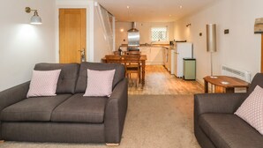 A modern living room with two grey sofas, a wooden dining table, and a kitchen in the background. - The Mistal (Keighley)