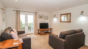 A living room with two sofas, a TV on a wooden stand, and a sliding glass door leading to a balcony. - The Mistal (Keighley)