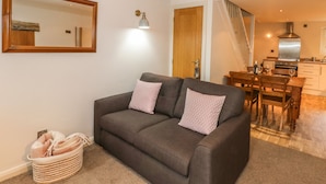 A modern living room with a grey sofa, two patterned cushions, a wooden coffee table, and a dining area with a wooden table and chairs. - The Mistal (Keighley)