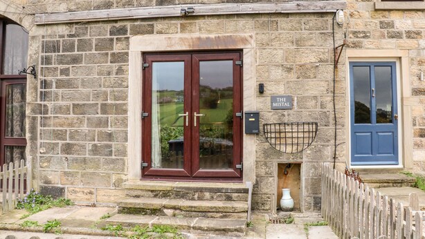 A stone building with a wooden door and a blue door. There is a sign that reads "The Mistal." - The Mistal (Keighley)