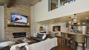 A spacious living room with a fireplace, a large TV mounted on a brick wall, and a bar area with stools. - Majestic Mountain Retreat | AC, Pool, Hot Tub, Golf & Ski (Durango)