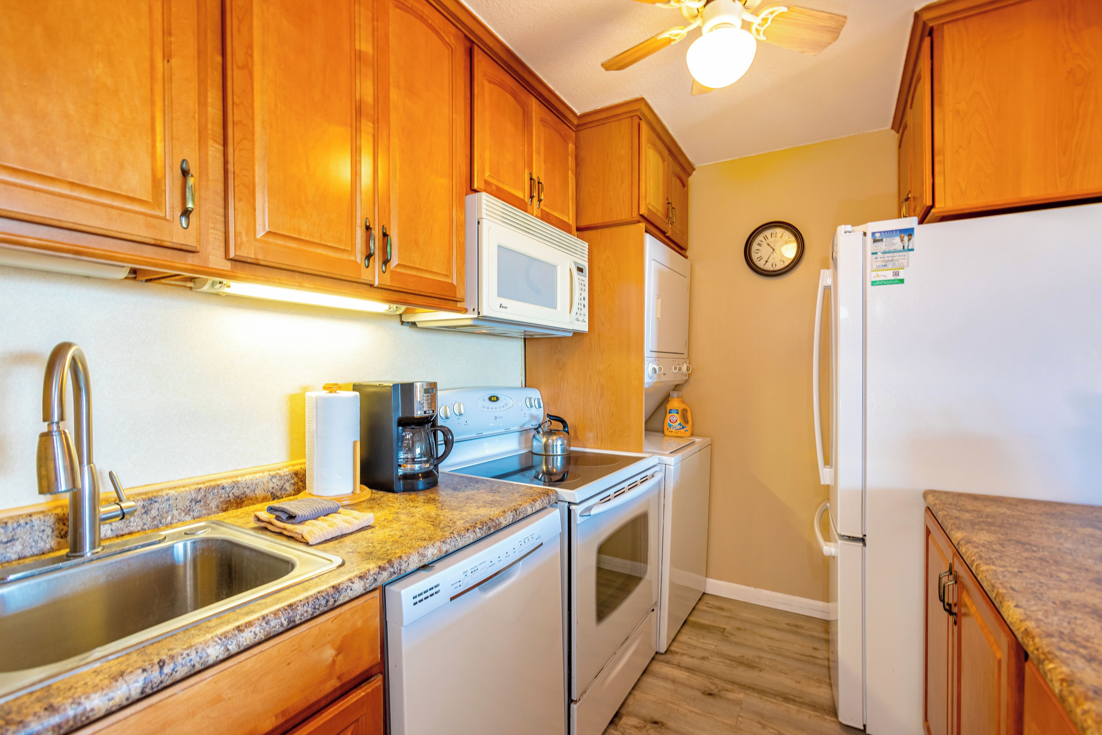 Una cocina con armarios de madera, microondas, estufa, lavamanos y refrigerador.