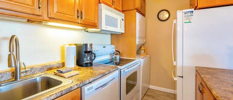Una cocina con armarios de madera, microondas, estufa, lavamanos y refrigerador.