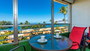 Varanda com mesa de vidro, duas cadeiras vermelhas e vista para o oceano e edifícios do resort.