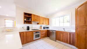 A modern kitchen with wooden cabinets, a gas stove, a microwave, and a dishwasher. - Ruby's Place is a unique beach house with all the creature comforts of home (Black Head)