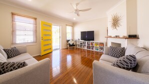 A living room with a flat-screen TV, a fireplace, and a bookshelf. - Ruby's Place is a unique beach house with all the creature comforts of home (Black Head)