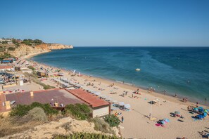 Une plage dotée de nombreux parasols et de chaises longues, une rive sablonneuse et une mer d’un bleu limpide.
