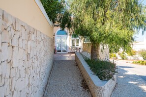 A narrow stone pathway leading to a building entrance with a tiled patio and outdoor seating. - 3 Bed/2 bath apt, terraces, pool, walk to beach (Lagos)