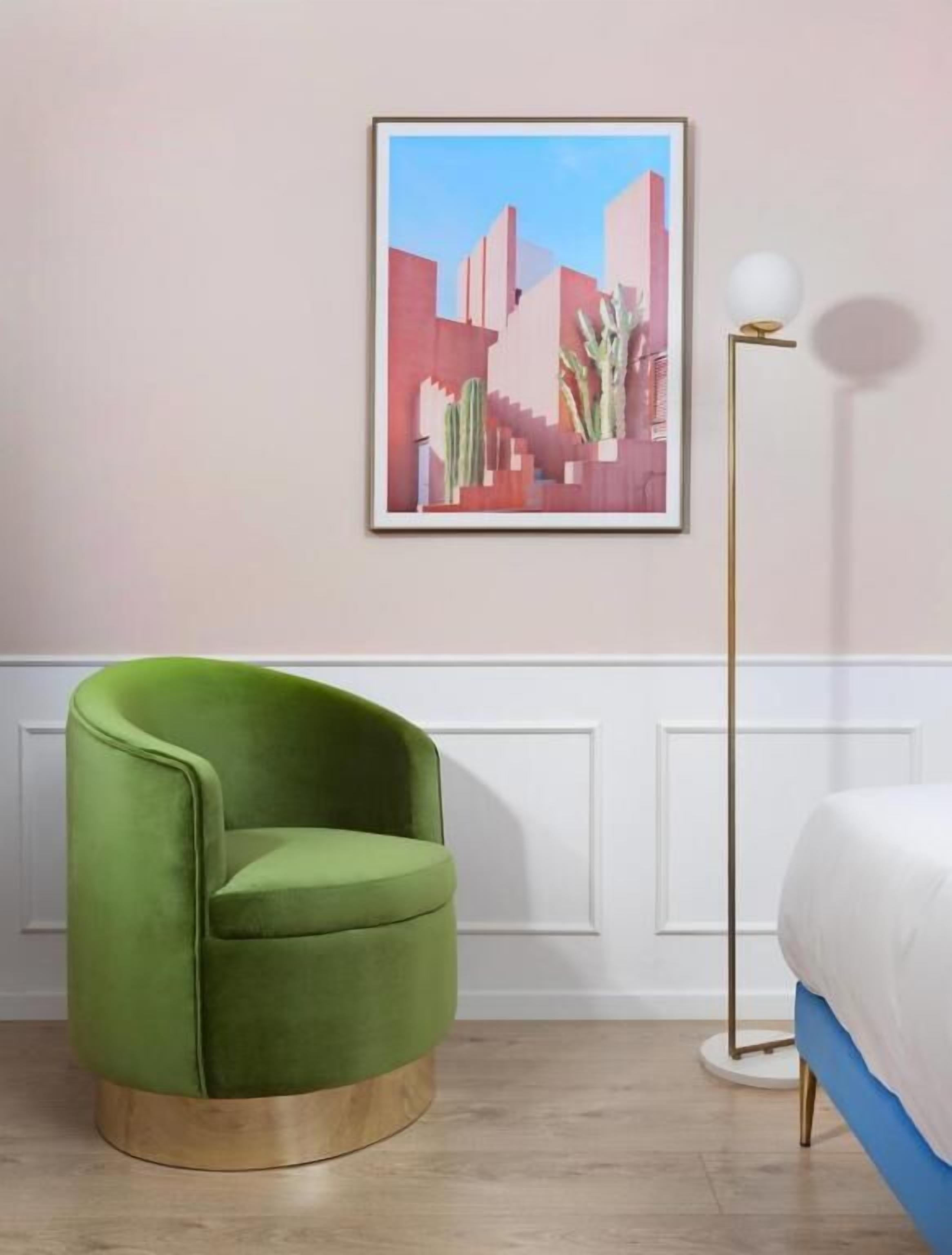 A room with a green armchair, a bed with white bedding, a floor lamp, and a framed picture on the wall.