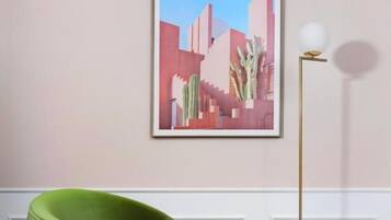 A room with a green armchair, a bed with white bedding, a floor lamp, and a framed picture on the wall.