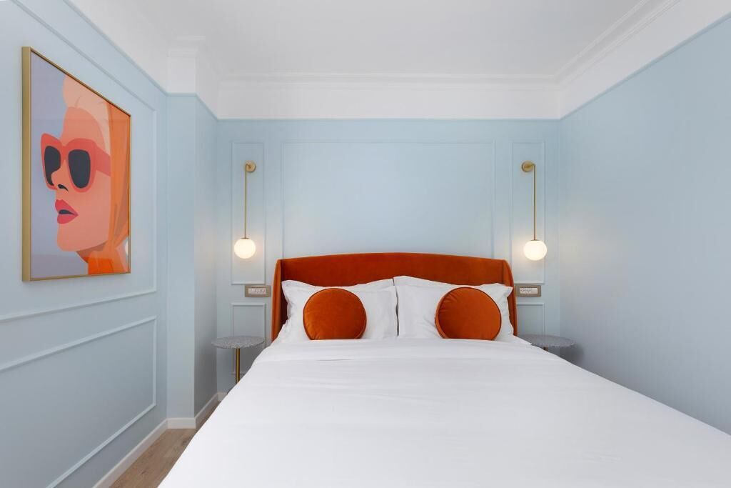 Un dormitorio con una cama, dos lámparas de pared y una obra de arte enmarcada en la pared.