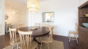 Un coin repas comprenant une table ronde, des chaises en bois, un luminaire en fibres tressées, un miroir et un meuble en bois.
