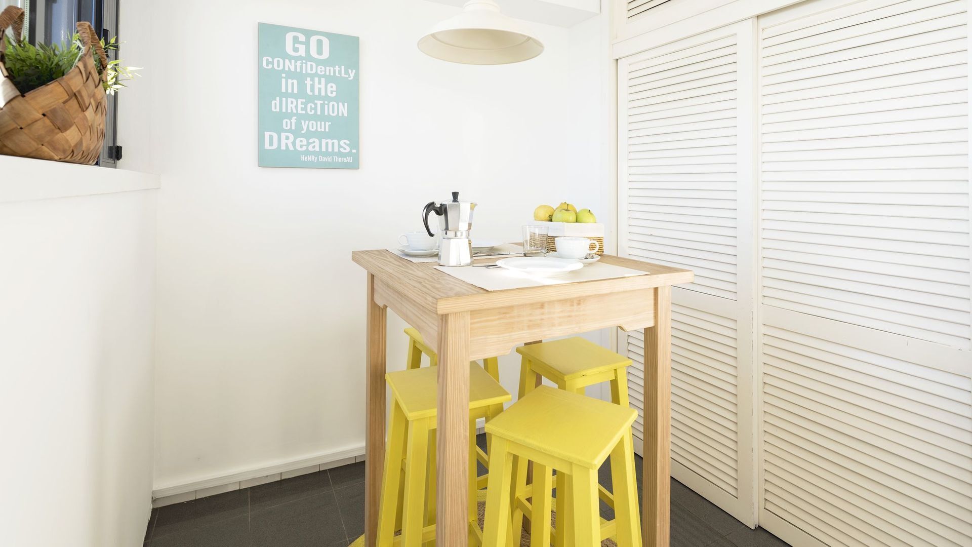 A small dining area with a wooden table, yellow chairs, and a wall-mounted sign.