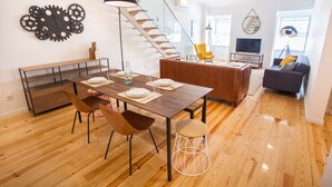 Un espacio habitable moderno con comedor, sofá, televisor y escalera.