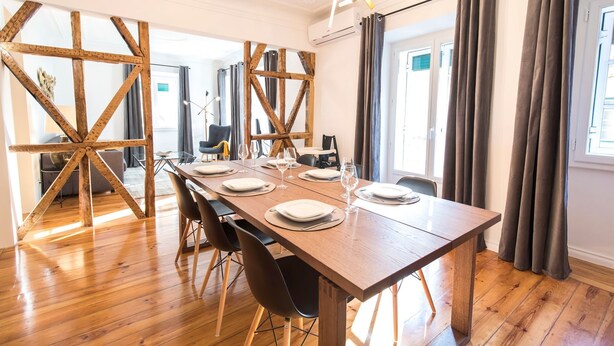 Un coin repas avec une table en bois dressée pour six personnes, entourée de chaises, et offrant une vue sur l’extérieur grâce à de grandes fenêtres.