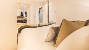 Une chambre d’hôtel moderne dotée d’un grand lit, d’un coin salon séparé avec un canapé et d’une vue sur une autre chambre grâce à un mur miroir.