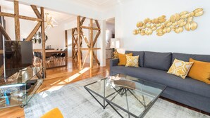 Un salon moderne avec une table basse en verre, un canapé gris agrémenté de coussins jaunes et une structure de plafond en bois.