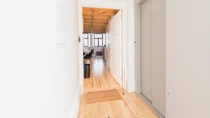 Un corridoio stretto con pavimento in legno che conduce a una stanza con una finestra e una porta.