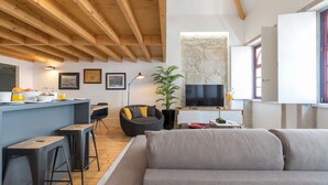 Un soggiorno moderno con soffitto in legno, un divano grigio, una poltrona nera, una TV e una parete in pietra.