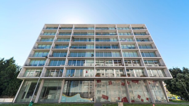 En byggnad med flera våningar och en modern arkitektonisk design, med en stor glasfasad och balkonger på varje våningsplan.