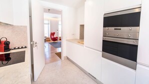 Une cuisine moderne avec des armoires blanches, un four encastré et une chaise rouge dans la pièce adjacente.