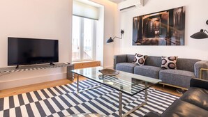 Un salon moderne avec un téléviseur à écran plat, une table basse en verre, un canapé gris agrémenté de coussins à motifs, un tapis rayé noir et blanc et un grand tableau abstrait accroché au mur.