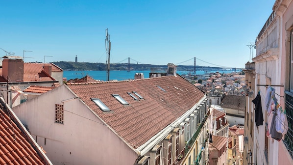 A view of a cityscape with a prominent bridge in the background, terracotta rooftops, and a clear blue sky. - Luxury Oasis in Bairro Alto by LovelyStay (Lisboa)